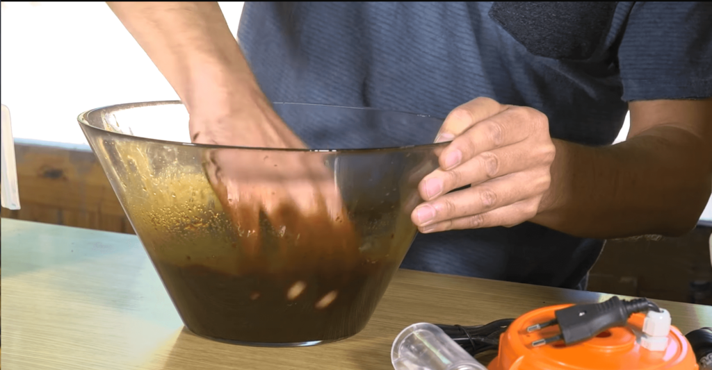 Una mano remueve un preparado casero de color marrón en un bol de cristal